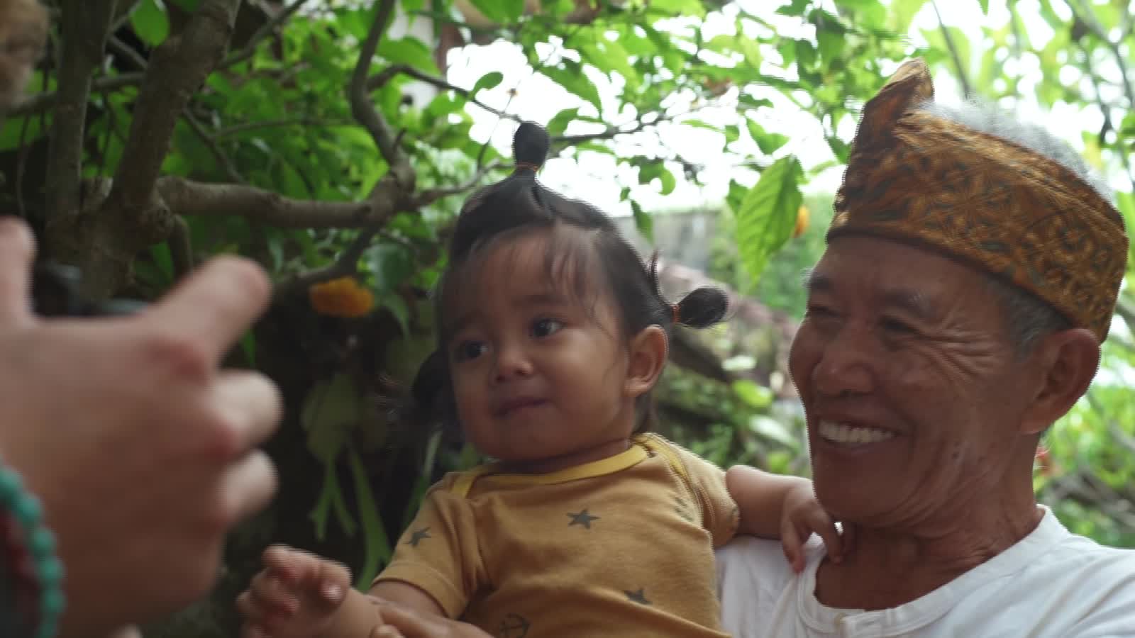 Wayan Pugur smiling while holding a small child.