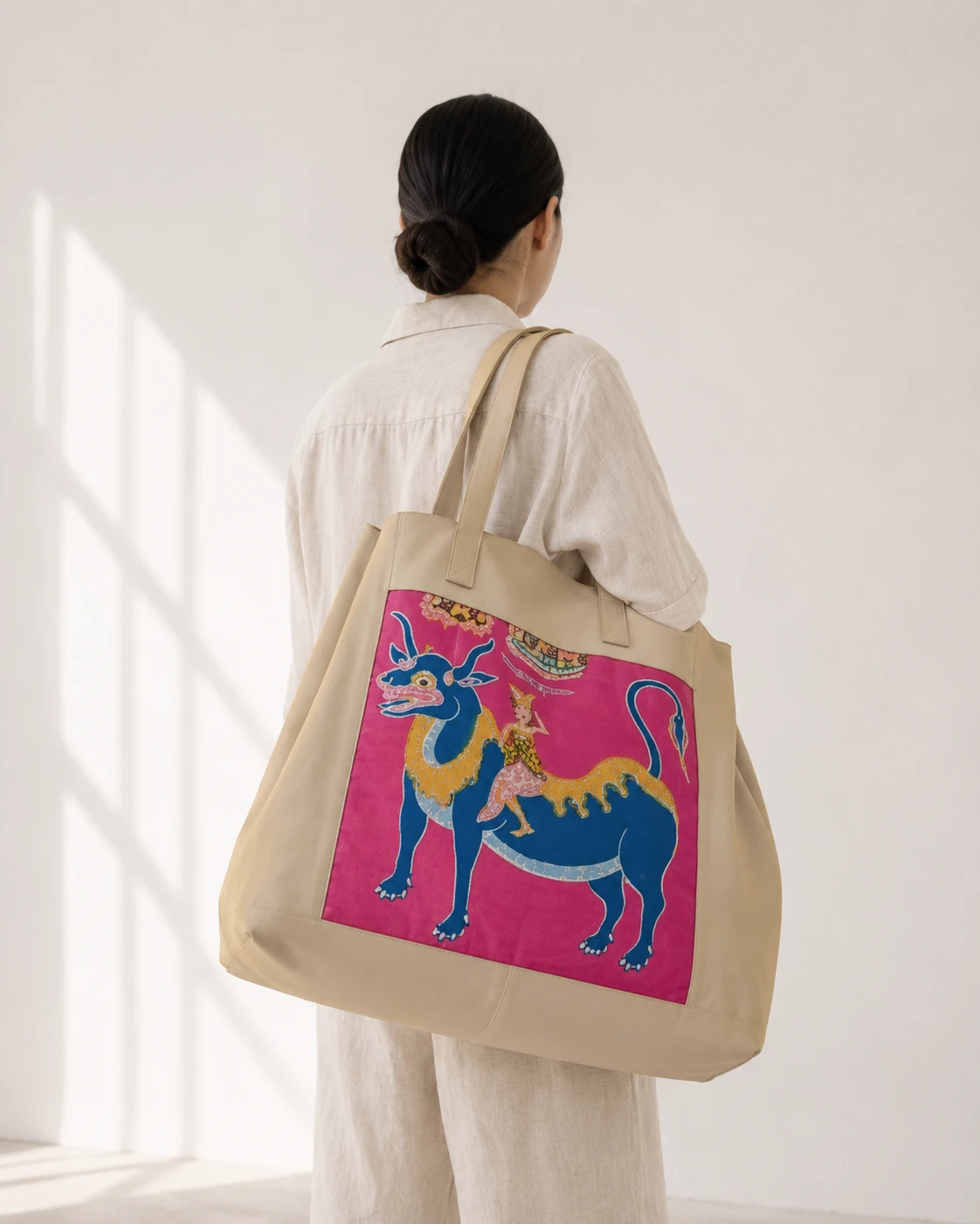 Oversized natural bag with a vivid pink and blue dragon painting panel, worn over white linen